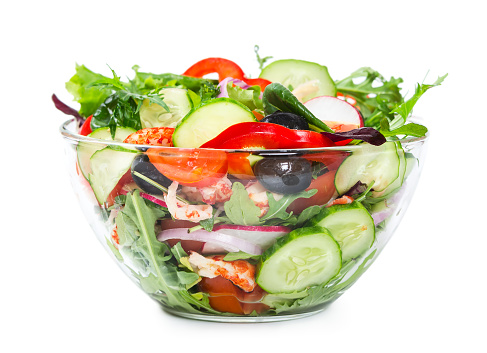 Salad with fresh vegetables, olives and shrimp in a glass bowl isolated on white background