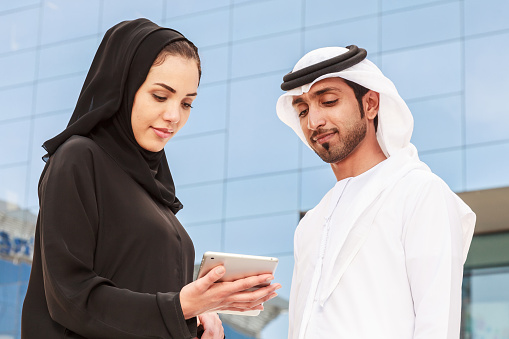 An arab business man and business woman are discussing a meeting on a tablet standing outdoor.