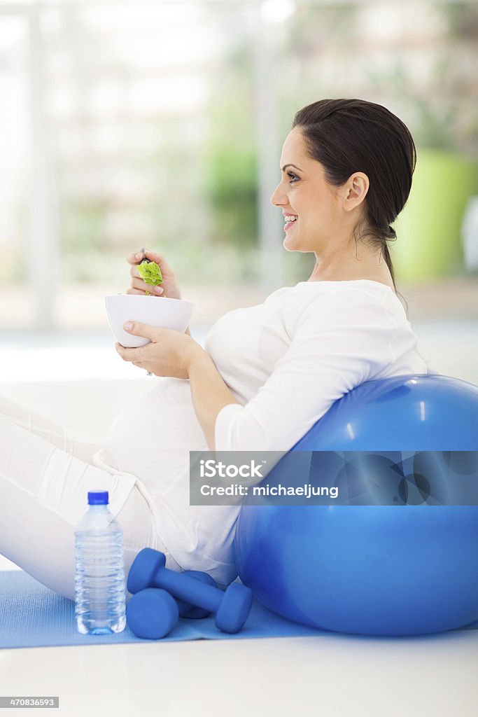 young pregnant woman holding bowl of green salad young pregnant woman holding bowl of green salad on exercise mat Adult Stock Photo