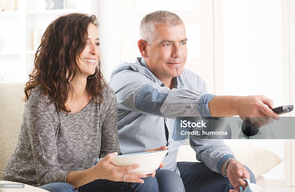 Couple watching tv in their living room Cheerful mature couple sitting together and watching TV Active Seniors Stock Photo