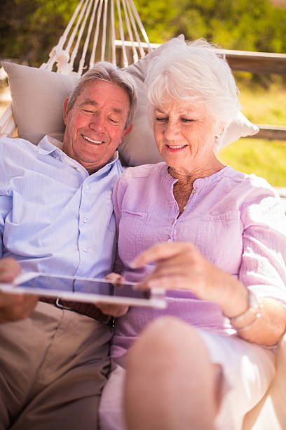 Senior couple using a digital tablet together Smiling senior couple sitting close together and using their digital tablet hammock men lying down digital tablet stock pictures, royalty-free photos & images