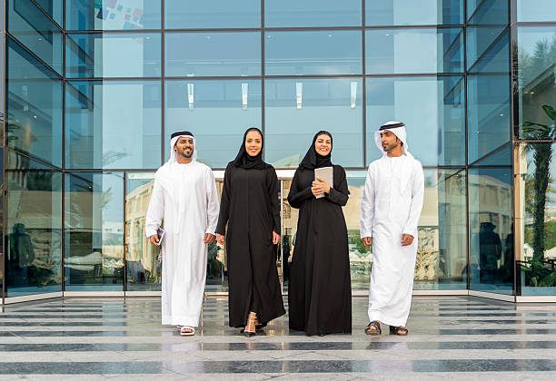 Young business people walking out of glass building Emarati Business people outside the office in Dubai, United Arab Emirates. united arab emirates photos stock pictures, royalty-free photos & images