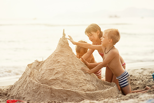 Brothers and sister having fun building a huge sandcastle on the beach.