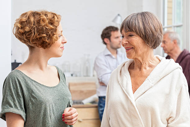 Daughter in Law Seeks Advice from Mother in Law A wife seeks advice from her mother-in-law first thing in the morning while her husband and father-in-law are in the background. father in law stock pictures, royalty-free photos & images