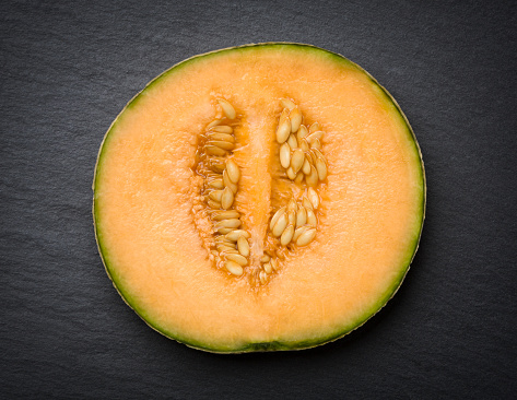 Sugar melon cut in half looking healthy and delicious, isolated on dark slate stone slab.