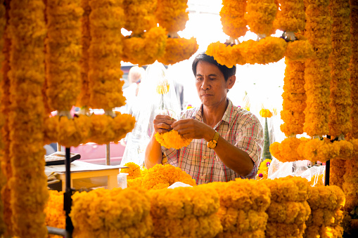 Thai florist vendor making Thai garlands for sale in a flower market located in Bangkok, Thailand.