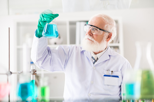 Bearded aged researcher looking at the flask in his hand