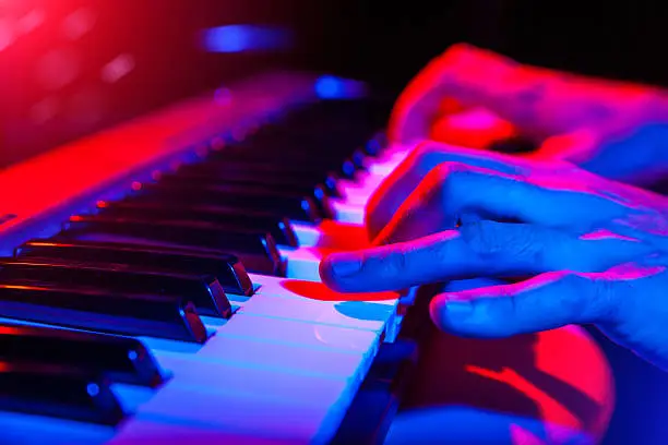 Photo of hands of musician playing keyboard in concert with shallow depth