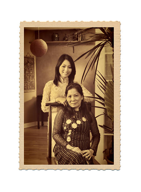 Old Photo of Asian Vietnamese Family in Traditional Home A retro antiqued old postcard photo of a traditional vietnamese Asian family. A mother and daughter two generations portrait set in a traditional Asian home with Asian decor and furnishing. Formal portrait with both subjects looking at camera smiling in traditional Vietnamese clothing. Photograph in deco edge border and sepia desaturated tone. vietnamese culture photos stock pictures, royalty-free photos & images