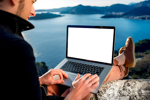 Man working with laptop on the top of mountain with beautiful landscape on background.