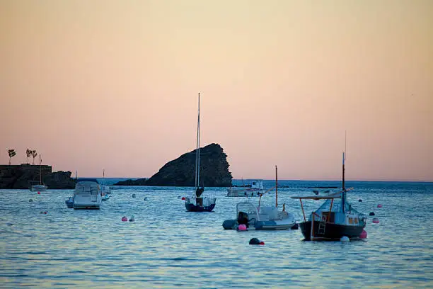 Cadaques sunset, boats in the bay, strange color in  the sky and the Rock  Es Cucurucuc in the center part of the image.