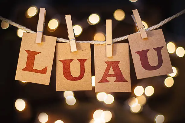 The word LUAU printed on clothespin clipped cards in front of defocused glowing lights.
