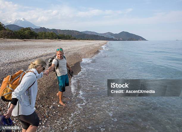 Man Extends Helping Hand To Woman On Pebble Beach Stock Photo - Download Image Now - 2015, 50-54 Years, A Helping Hand