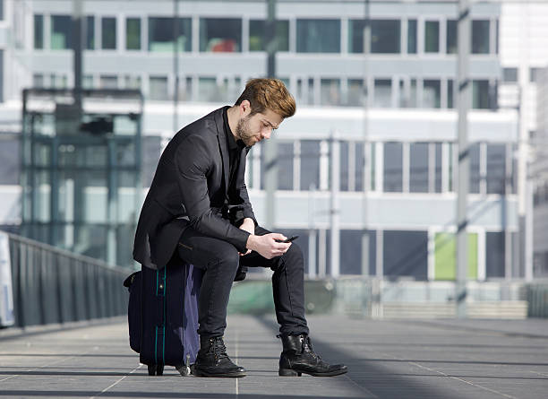 istock Male traveler sitting on suitcase reading text message 470958834