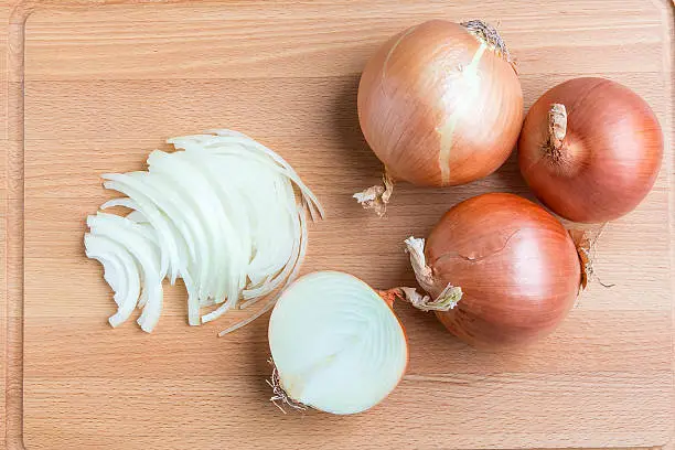 Photo of Whole and sliced onions on wooden cutting  board