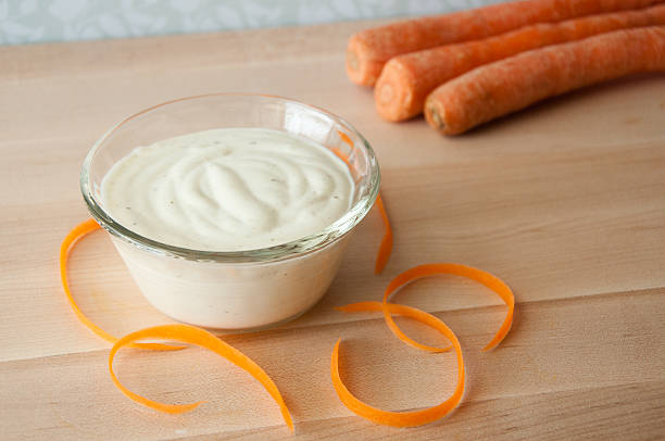 carrot shaving with ranch dressing unpeeled carrots in background; ranch dressing in a dish with carrot shavings on a cutting board in foreground ranch dressing stock pictures, royalty-free photos & images