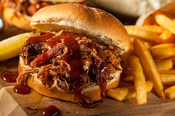 Barbeque pulled pork sandwich and fries on wooden board Barbeque Pulled Pork Sandwich with BBQ Sauce and Fries shredded photos stock pictures, royalty-free photos & images