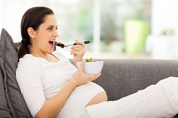 istock pregnant woman eating vegetables on sofa 470968163
