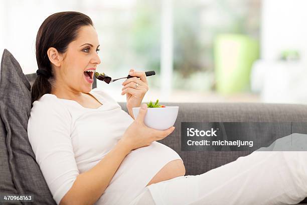 Pregnant Woman Eating Vegetables On Sofa Stock Photo - Download Image Now - Abdomen, Adult, Adults Only