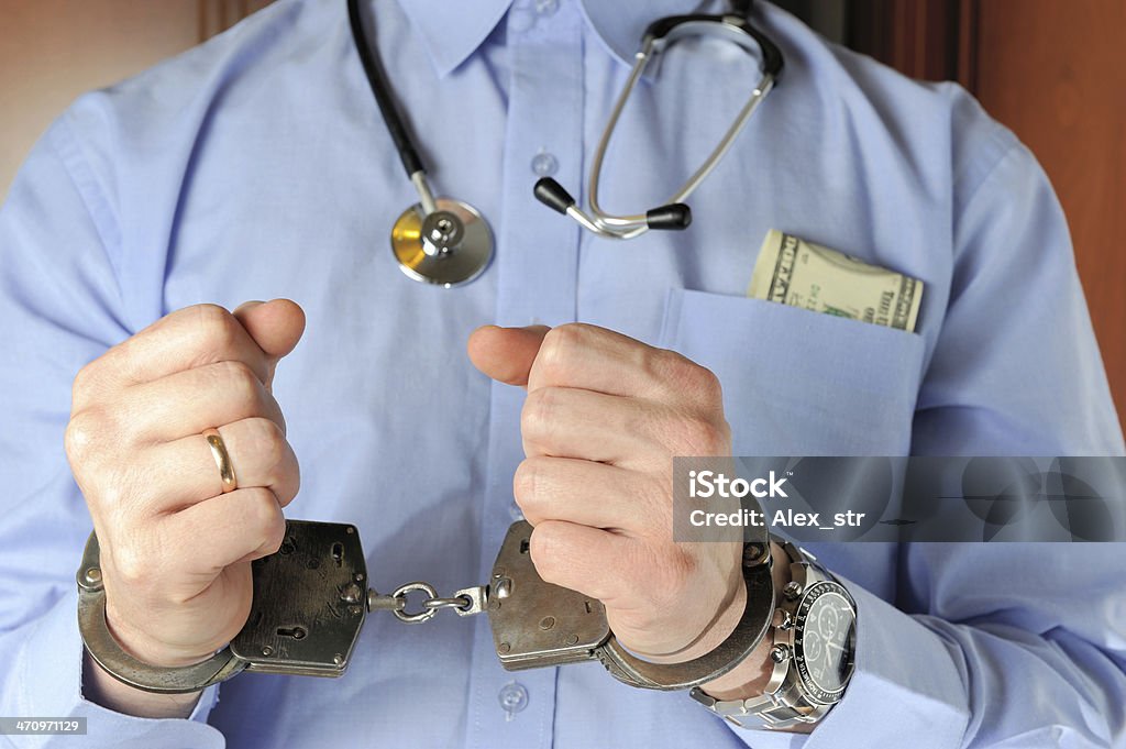 Man with stethoscope holds his hands in handcuffs before itself Man with stethoscope holds his hands in handcuffs before itself with money in the pocket Adult Stock Photo