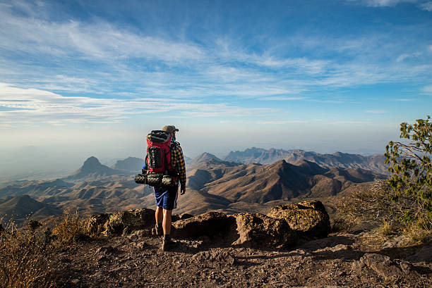 Hiker Stands on a Cliff A man pauses at the top of a steep cliff overlooking the Mexican border in Big Bend National Park, Texas texas mountains stock pictures, royalty-free photos & images