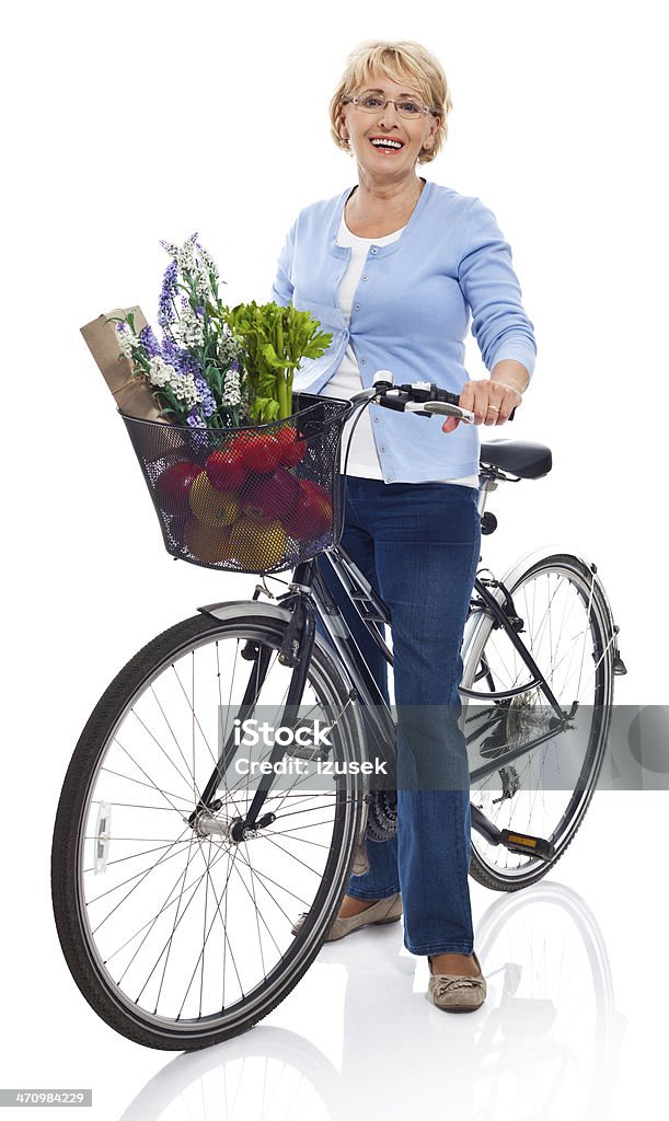 Active senior woman Portrait of smiling senior woman standing next to bicycle with grocery shopping in the basket. Studio shot, white background. Bicycle Stock Photo