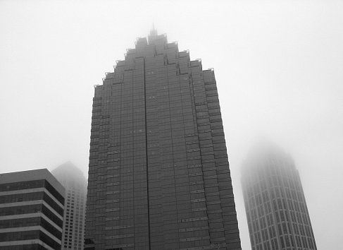 An upward shot of buildings towering into the fog. Part of the Atlanta skyline.