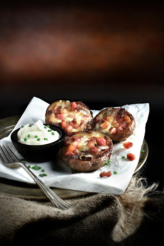 Creatively lit and selectively focused image of fresh baked Tex-Mex potato skins with melted cheese, bacon and soured cream against a dark, rustic background. Copy space.