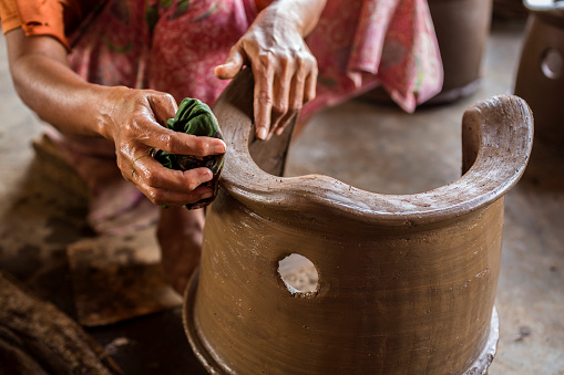 A senior lady of Asian origin is polishing with a mix of water and coconut oil lotion the brand new pottery she just finished making. In remote places of Asia, local people still prefer working by hand rather than machinery.
