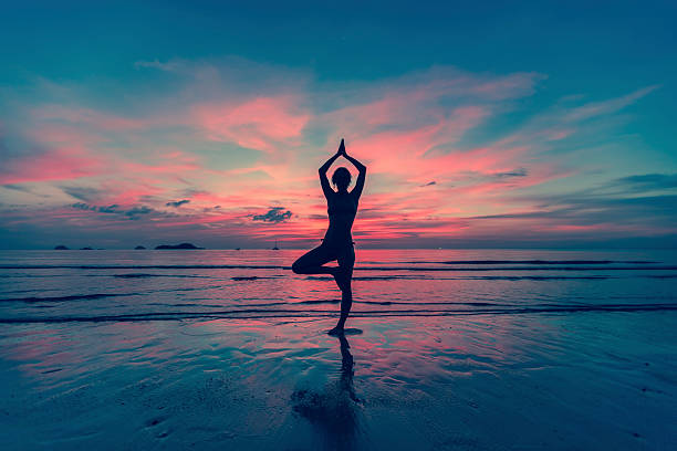 istock Silhouette young female practicing yoga on the beach at sunset 470992320