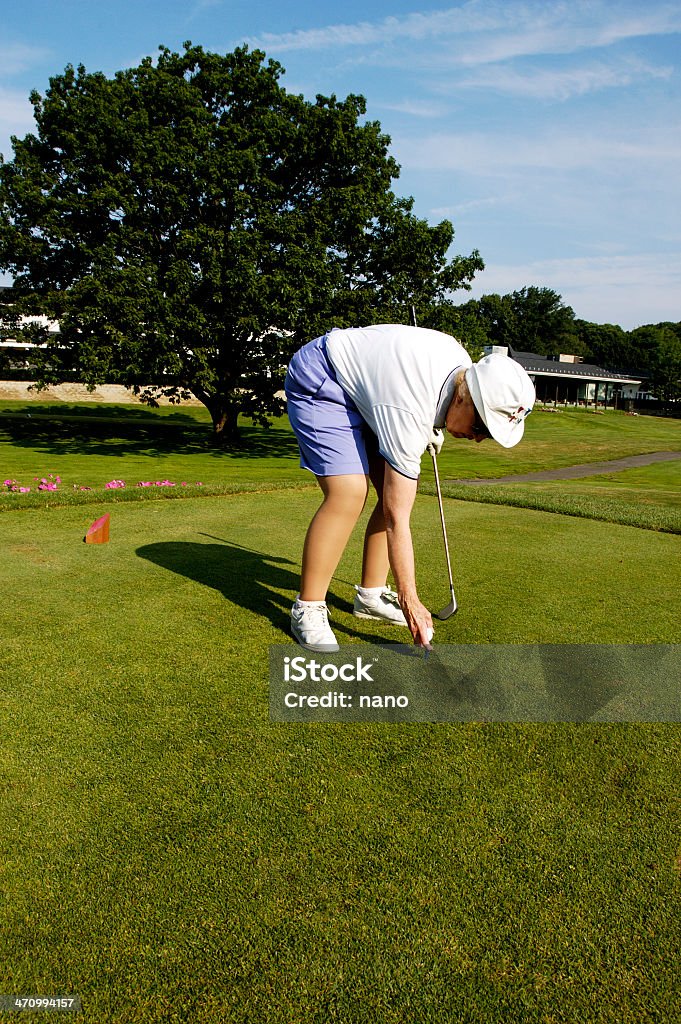 inserting a tee Senior woman bending over to insert a tee on the green. 80-89 Years Stock Photo