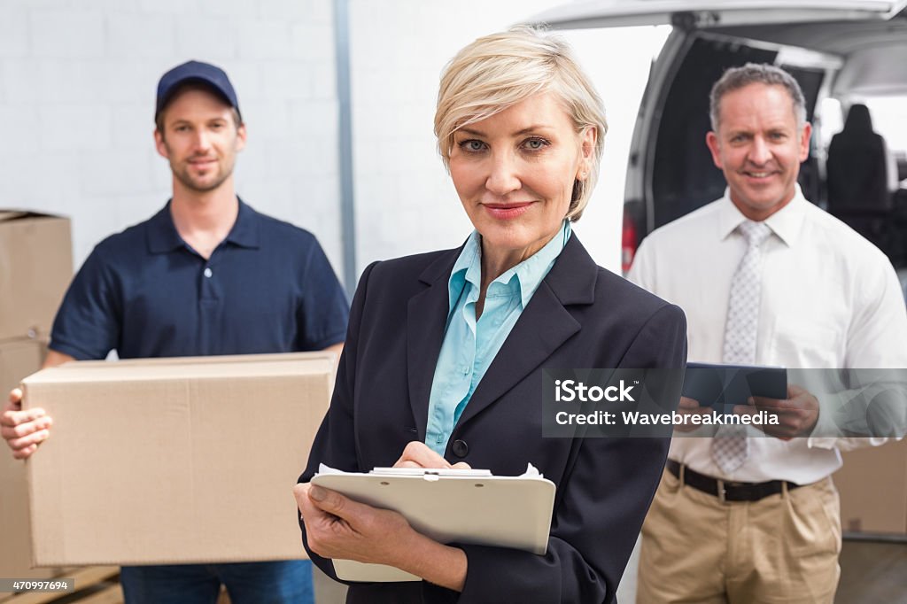 Smiling manager holding clipboard in front of his colleagues Smiling manager holding clipboard in front of his colleagues in a large warehouse 20-29 Years Stock Photo