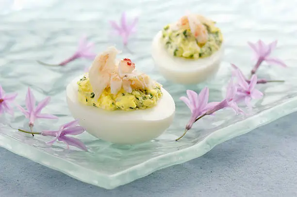 Tight shot of deviled eggs topped with crab meat on a glass plate accented by small lavender flowers.