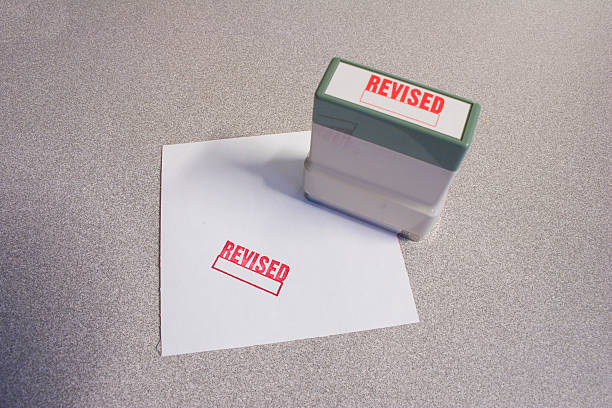 "Revised" Stamp and Paper "Revised" stamped on paper and stamper in red.   Part of a series. revised stock pictures, royalty-free photos & images