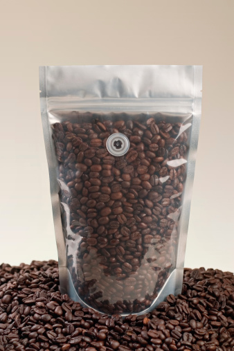 A designer friendly clear coffee pouch surrounded by delicious roast coffee beans.  Ready for your spiffy label and label design!