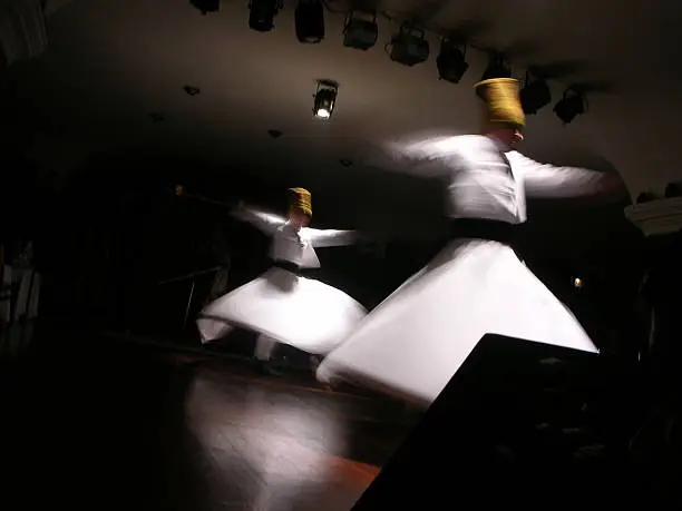 Whirling Dervishes in white and in a religious trance performing on a Turkish stage.