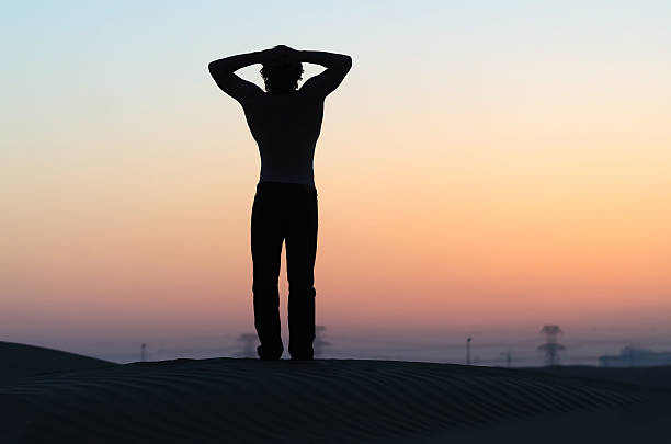 istock Man silhouette at sunset in desert with hands behind head 471015532