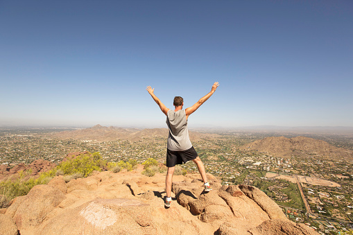 This image is taken while climbing to the top of Camelback Mountain in Arizona. The rocky terrain overlooks Scottsdale. Landscape scenery is speckled with cactus and small shrubs. The sky is blue with hot sunshine. Image taken in April. Image can be used as a leadership analogy of achieving success with determination through challenging experiences.