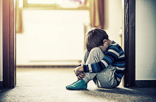 Depressed little boy sitting on the floor Depressed sad child sitting on the floor, in the door. The little boy is hiding his head between legs. orphan stock pictures, royalty-free photos & images