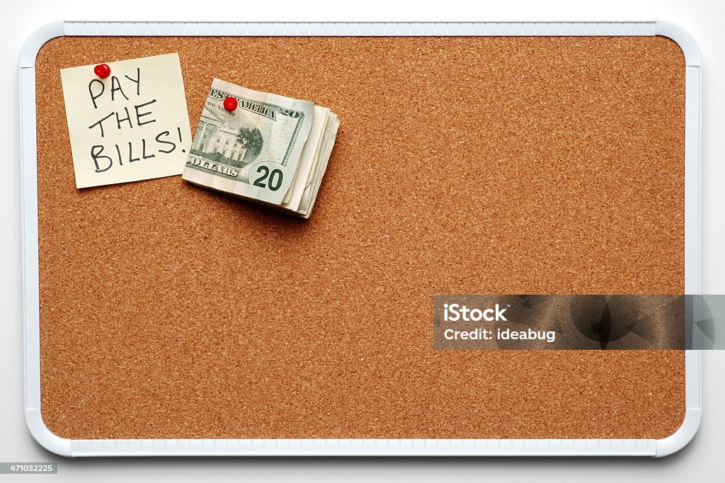 Remember to Pay the Bills! Color photo of a bulletin board isolated on white with a post-it note reading "Pay the Bills!" and a wad of money posted on it. Adhesive Note Stock Photo