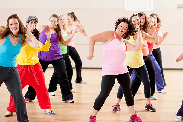 A group of women at different fitness levels working out and dancing together during a class in a gym studio.