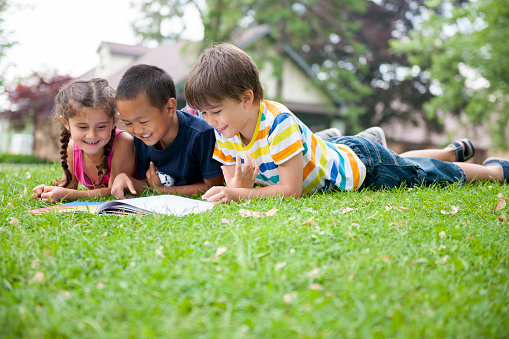 Elementary aged children reading a book in the park.