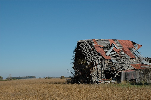 Rural barn on a family farm that has fallen into disrepair.  Equipment and straw bales have tumbled out of the barn.