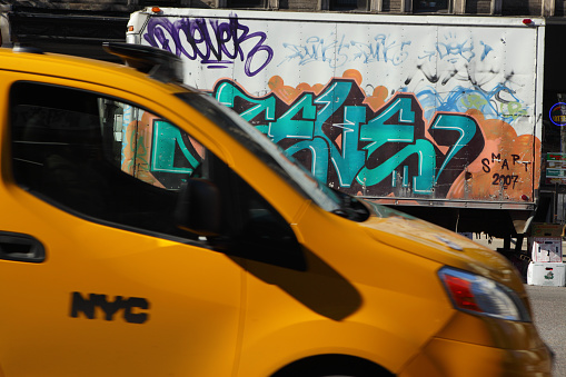New York, NY, USA - April 22, 2015: A yellow taxi cab passes a colorful graffiti covered panel van parked on Kenmare Street on the Lower East Side of Manhattan. The truck is parked at the north end of Chinatown and Little Italy and is filled with vegetables and fruit being delivered to the local stores. Many of the delivery vans in the area are covered in graffiti like this one.