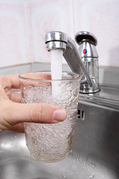 istock hand pours water into a glass from kitchen faucet 471048468