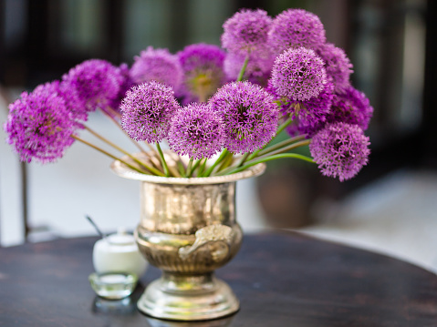 Allium flowers bouquet in a stylish metal decorative vase - selective focus, very shallow deep of field; creamy background