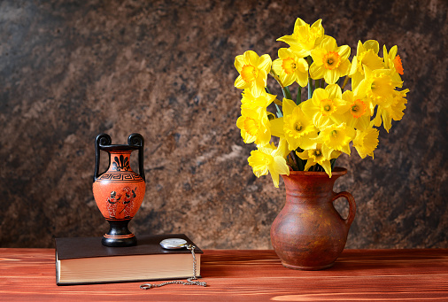  Yellow daffodils in a ceramic vase, amphorae and books on the table