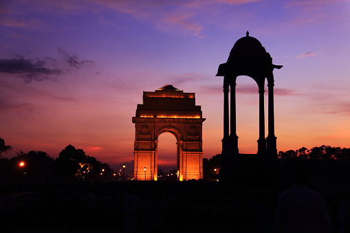 Image of the very famous landmark in Delhi-India, the India Gate. The image has been shot during dusk, while the monument was illuminated by artificial lights. The evening lights of the sun casts an orange tone in the sky. 
