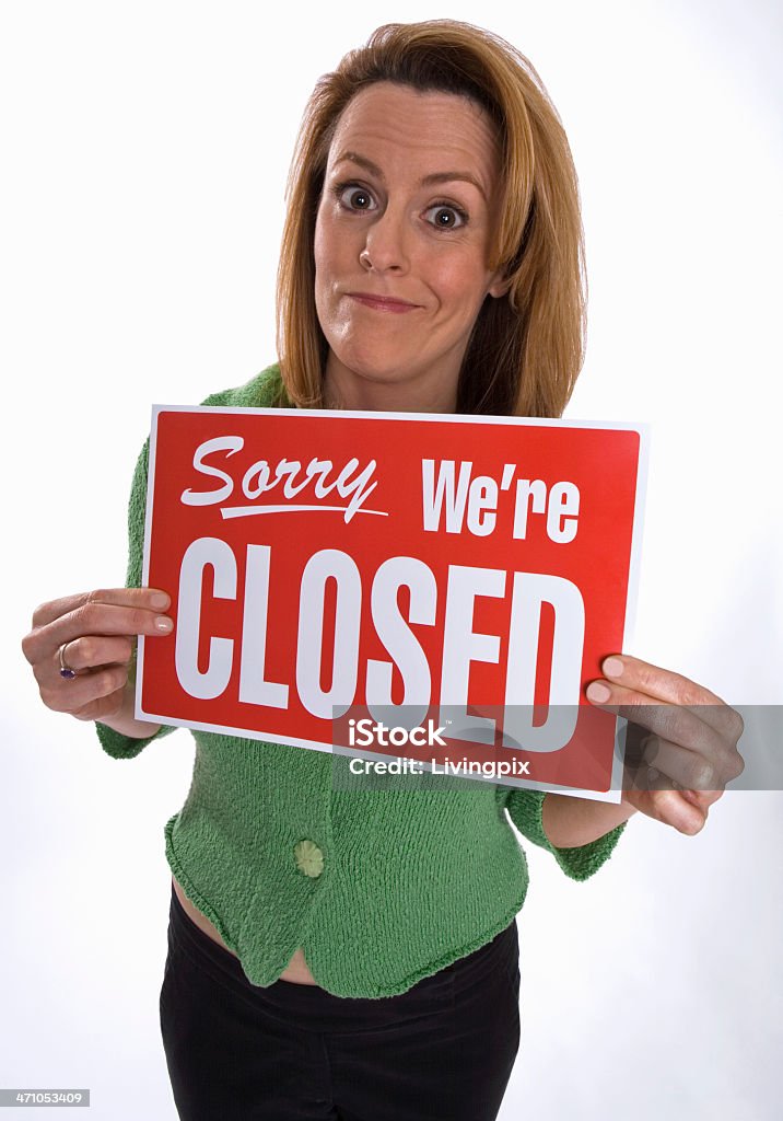Young woman holds up "Sorry We're Closed" sign A young redheaded woman holds up a red and white "Sorry We're Closed" sign while looking into the camera with a resigned smile. Adult Stock Photo