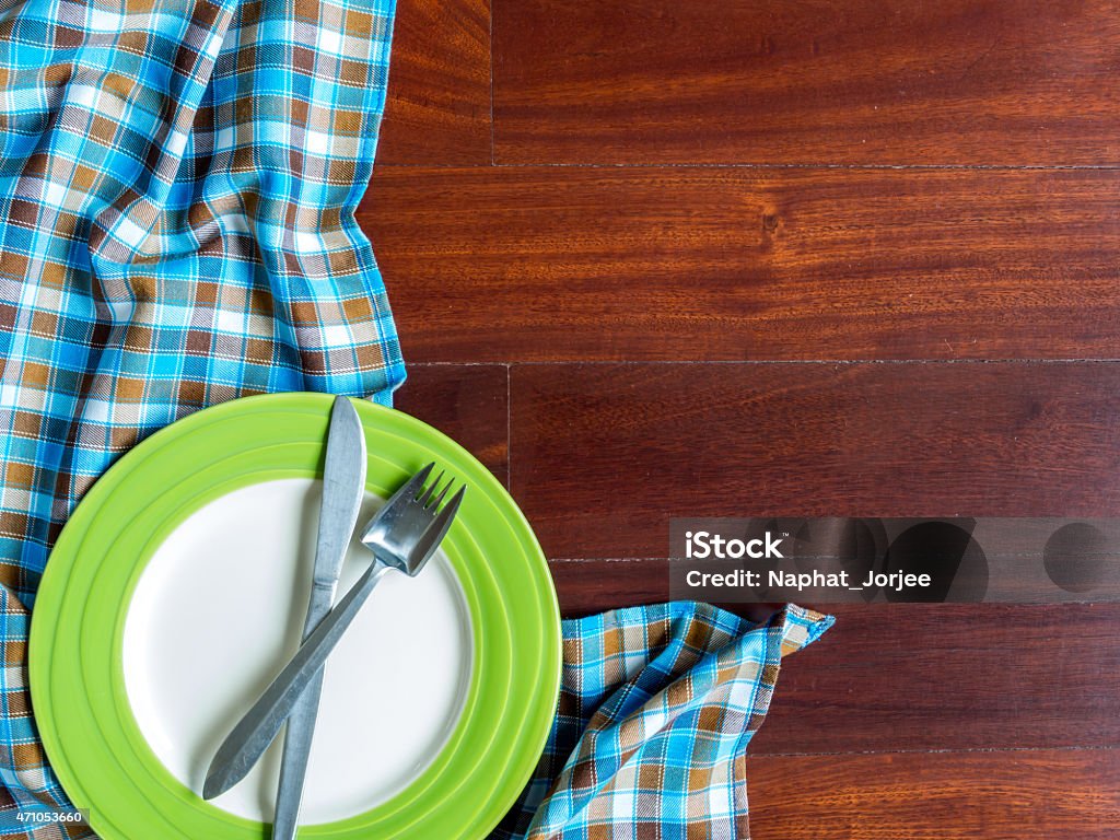 Blank plate with fork and knife on wooden table background Blank plate with fork and knife on checked tablecloth over wooden table background 2015 Stock Photo